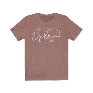 May include: A heather brown t-shirt with the text "Half my heart is Deployed" in white cursive lettering.