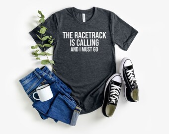 May include: A dark grey t-shirt with the text "The racetrack is calling and I must go" in white lettering.