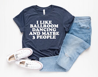 May include: A navy blue t-shirt with white text that reads "I like ballroom dancing and maybe 3 people". The shirt is laid flat on a white surface with a pair of white sneakers and blue jeans.