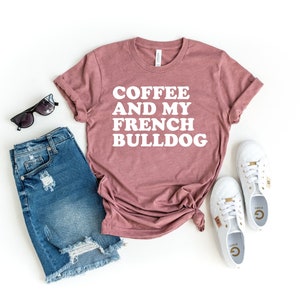 Puede incluir: Una camiseta color malva con el texto "COFFEE AND MY FRENCH BULLDOG" en blanco. La camiseta est&aacute; colocada sobre un fondo blanco con un par de gafas de sol negras, un par de zapatillas blancas y un par de pantalones cortos de mezclilla azul.