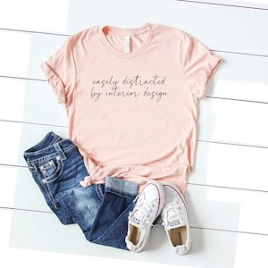 May include: A pink t-shirt with the text "easily distracted by interior design" in black script.