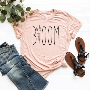 May include: A light pink t-shirt with a black graphic that says "BOOM" with a stylized flower design.