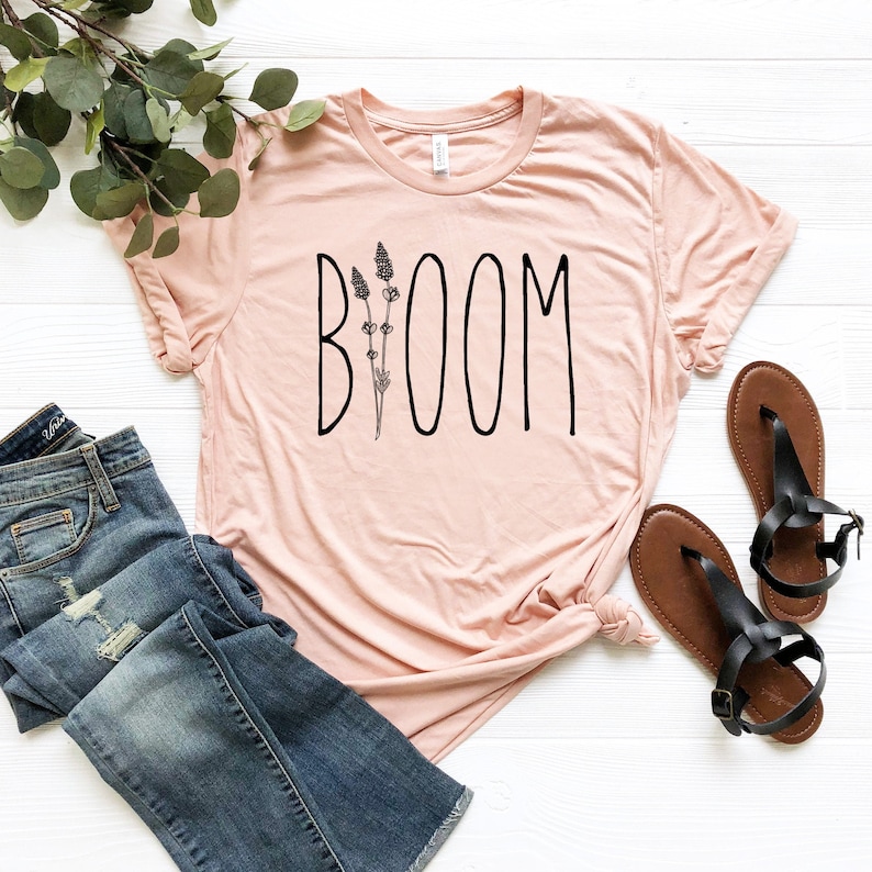 May include: A light pink t-shirt with a black graphic that says "BOOM" with a stylized flower design.