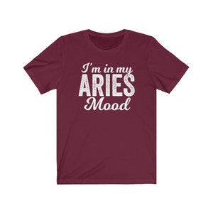 以下が含まれることがあります： 白文字で「I'm in my ARIES Mood」と書かれた、ワインレッドの半袖Tシャツです。
