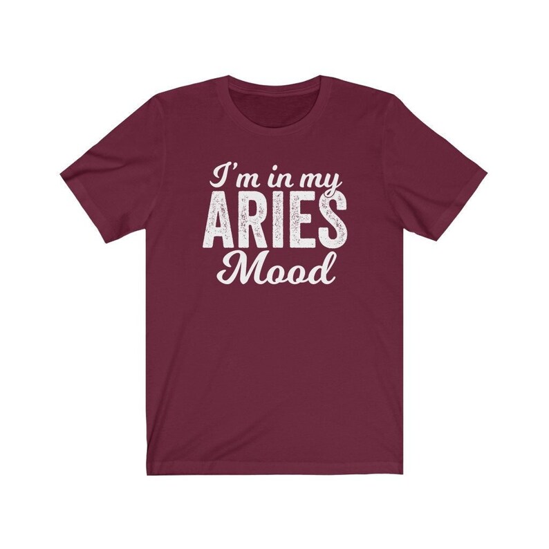 以下が含まれることがあります： 白文字で「I'm in my ARIES Mood」と書かれた、ワインレッドの半袖Tシャツです。