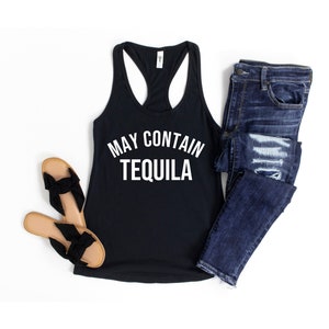 Puede incluir: Camiseta de tirantes negra con texto blanco que dice "May Contain Tequila". La camiseta de tirantes se combina con pantalones vaqueros azules y sandalias marrones.