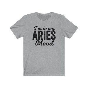 以下が含まれることがあります： グレーのTシャツに黒い文字で「I'm in my Aries Mood」と書かれています。