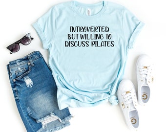 May include: A light blue t-shirt with the text "Introverted but willing to discuss Pilates" in black lettering.