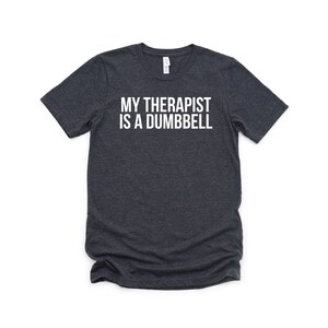 Puede incluir: Camiseta gris oscuro jaspeada con texto blanco que dice "Mi terapeuta es una mancuerna".