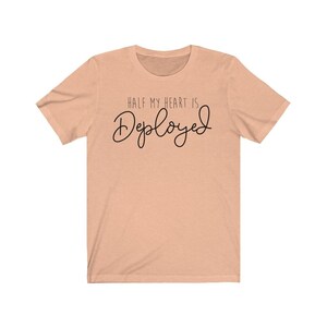 May include: Peach-colored t-shirt with the text "Half my heart is Deployed" in black script.