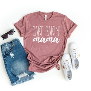 May include: A mauve t-shirt with the text "Cake Bakin' mama" in white lettering.