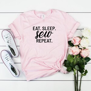Könnte beinhalten: Rosa T-Shirt mit dem Text "Eat. Sleep. Sew. Repeat." in schwarzer Schrift.