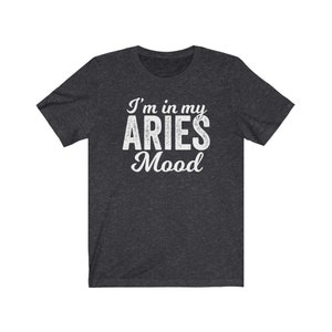 以下が含まれることがあります： 暗いヘザーグレーのTシャツに、白い文字で「I'm in my Aries Mood」と書かれています。