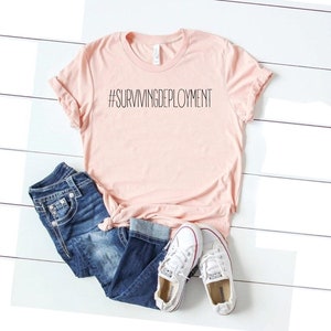 May include: A pink t-shirt with the text "#SURVIVINGDEPLOYMENT" printed in black.