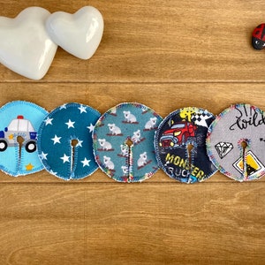 Könnte beinhalten: Fünf runde Stoff-Stillkissen mit verschiedenen Designs. Die Designs beinhalten ein Polizeiauto, Sterne, Koalas, einen Monstertruck und einen Diamanten mit dem Wort "wild".