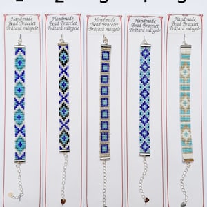 Può includere: Cinque braccialetti di perline fatti a mano con diversi motivi geometrici in blu, bianco e oro. I braccialetti sono su carte bianche con il testo "Handmade Bead Bracelet Brățară mărgele" e "România Sibiu Handmade".