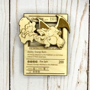May include: Wooden Charizard Pokémon card with a 3D cutout design. The card features the text "Charizard" and "LV.76", along with the ability "Energy Burn" and the attack "Fire Spin". The card is made of light-colored wood.