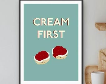 May include: A framed print featuring the words "CREAM FIRST" in a retro font, set against a teal background. Below the text are two illustrations of scones topped with jam. The print is in a black frame.
