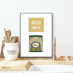 May include: A white framed print with a gold background and the text "HELLO SWEETIE" in white. Below the text is a green and gold illustration of a Lyle's Golden Syrup can.