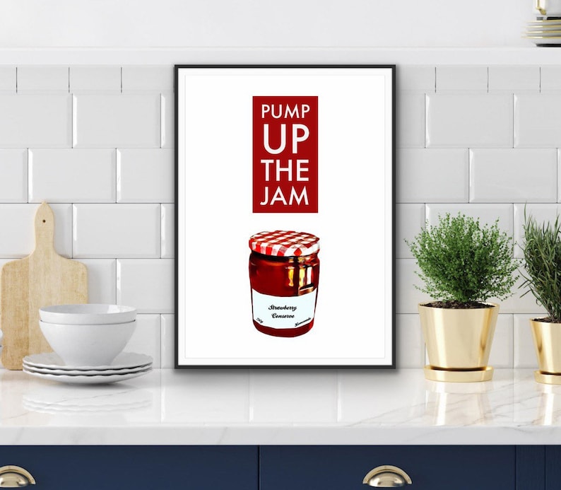 Puede incluir: Una impresi&oacute;n enmarcada que presenta un tarro de conserva de fresa con una tapa a cuadros rojos y blancos. El texto "PUMP UP THE JAM" est&aacute; encima del tarro en un rect&aacute;ngulo rojo. El tarro tiene una etiqueta blanca que dice "Strawberry Conserve".