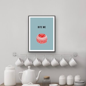 May include: A framed print with a light blue background and the text "BITE ME" in black. A red and white bottle cap is centered on the print.