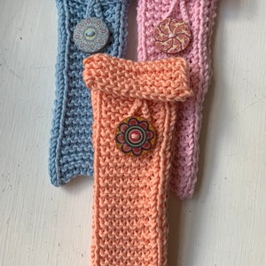 Peut inclure: Trois étuis à crayons tricotés avec des boutons de couleurs différentes. Les étuis sont bleu clair, rose et pêche. Les boutons sont tous ronds et ont des motifs différents.