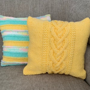 Pu&ograve; includere: Due cuscini di maglia, uno giallo con un motivo a treccia e l'altro a righe in giallo, azzurro e rosa.