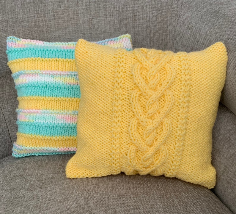 Pu&ograve; includere: Due cuscini di maglia, uno giallo con un motivo a treccia e l'altro a righe in giallo, azzurro e rosa.