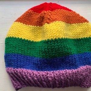 May include: A rainbow striped crocheted beanie hat with a purple brim.