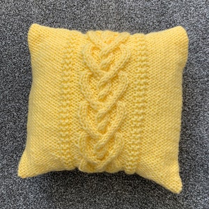 Pu&ograve; includere: Un cuscino di maglia giallo con un motivo a treccia.
