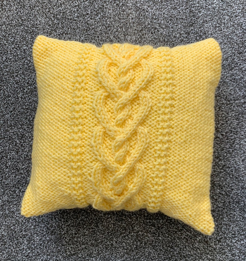 Pu&ograve; includere: Un cuscino di maglia giallo con un motivo a treccia.