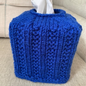 May include: A blue knitted tissue box cover with a cable knit pattern.