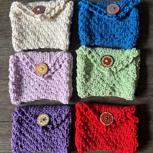 May include: Six handmade knitted coin purses in various colors: cream, blue, lavender, green, purple, and red. Each purse features a decorative wooden button closure. The purses are arranged on a wooden surface.