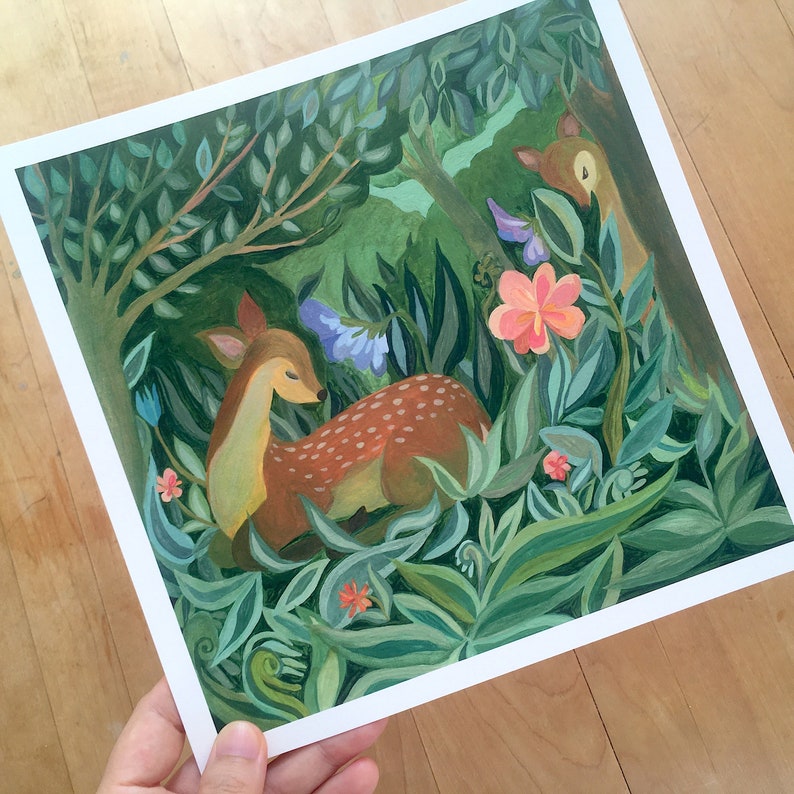 May include: A square art print featuring a painted scene of two deer resting in a lush forest. One deer lies in the foreground among green foliage, while another is partially visible behind a large pink flower and blue blossoms.
