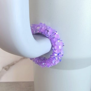 May include: A purple sparkly cup charm made of small beads. The charm is in the shape of a circle and is designed to fit around the handle of a cup.