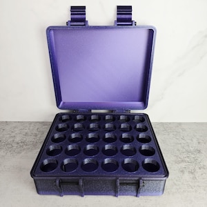May include: An open, purple carrying case with a grid of circular compartments. The case has a hinged lid and two latches. The interior is designed to hold small items, such as essential oil bottles or small tools. The case is made of a durable material.