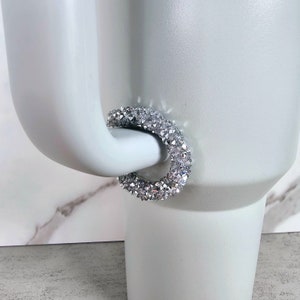 May include: A silver sparkly ring with a round shape. The ring is made of small, clear rhinestones that are clustered together.