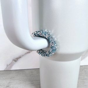 May include: A pair of hoop earrings made of small, light blue and silver rhinestones. The earrings are round and have a sparkly finish.
