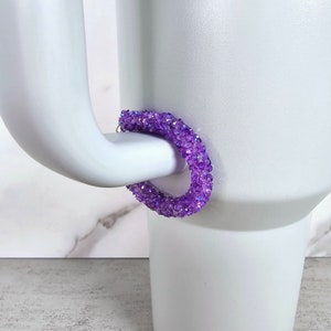 May include: Purple crystal hoop earrings. The earrings are made of small, iridescent crystals that are clustered together to form a hoop shape.