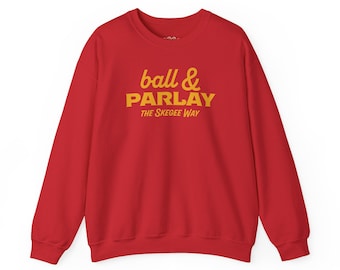 May include: A bright red long-sleeve crewneck sweatshirt featuring yellow text printed on the chest. The graphic displays the words ball & PARLAY in a mix of script and bold block lettering, followed by the text THE SKEGEE WAY below it.