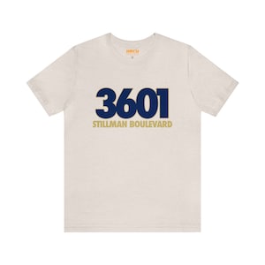 May include: A light beige t-shirt with a navy blue and gold graphic that says "3601 Stillman Boulevard".