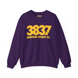 May include: A deep purple long-sleeve crewneck sweatshirt featuring large yellow text on the chest that reads 3837 SIMPSON STUART RD. The garment has a ribbed collar, cuffs, and hem, with a simple, clean design and a solid color background.