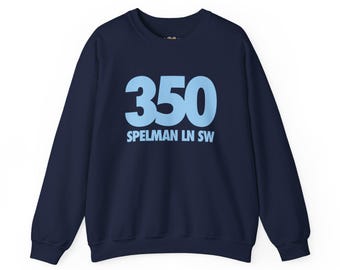 May include: A navy blue crewneck sweatshirt featuring the light blue text 350 and SPELMAN LN SW printed on the front. The garment has long sleeves, a ribbed neckline, and ribbed cuffs, providing a standard fit for casual wear.
