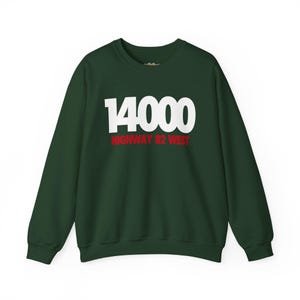 May include: A dark forest green crewneck sweatshirt featuring the white text 14000 centered on the chest, with the red text HIGHWAY 82 WEST printed directly underneath in a smaller, bold sans-serif font. The garment has long sleeves and ribbed cuffs.
