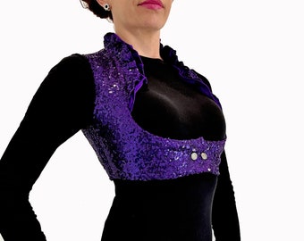 Può includere: Gilet di paillettes viola con colletto in velluto e due bottoni argentati. Il gilet è corto e ha una scollatura profonda.