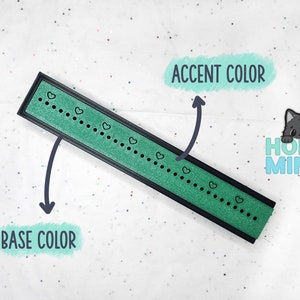 Puede incluir: Un objeto rectangular verde y negro con un borde negro y un patrón de pequeños puntos negros y corazones. El objeto está etiquetado como "ACCENT COLOR" y "BASE COLOR" en la imagen.