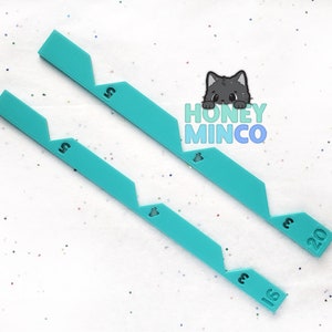 May include: Two turquoise plastic rulers with zig-zag edges and numbers 5, 15, and 20 printed on them.