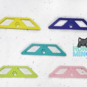 May include: Five plastic paw print shaped cat toys in different colors: yellow, purple, teal, green, and pink. The toys are shaped like a paw print with a hole in the middle.