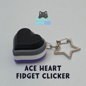 Può includere: Un fidget clicker a forma di cuore con i colori della bandiera del pride asessuale: nero, grigio, bianco e viola. Il clicker ha una parte superiore nera strutturata e un portachiavi a forma di stella argentata. Il testo sull'immagine recita "ACE HEART FIDGET CLICKER."