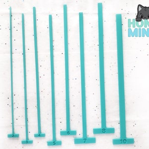 Op de afbeelding: Een verzameling turquoise, T-vormige gereedschappen, elk met een nummer van 2 tot 10 op de basis gedrukt. De gereedschappen zijn verticaal gerangschikt, waarbij de nummers van links naar rechts toenemen. Het Honey Minco-logo staat rechtsboven.